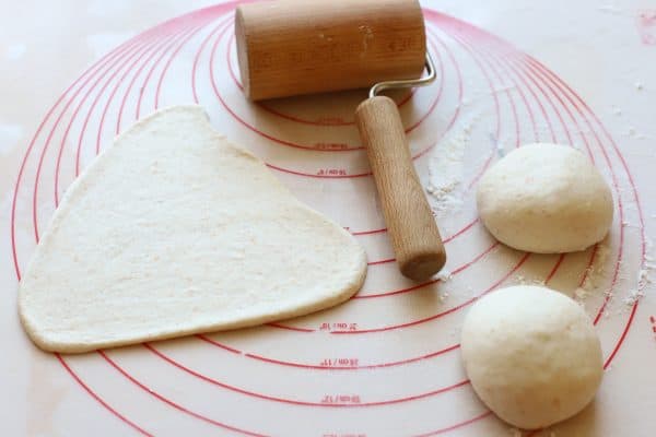 Z nakysnutých guličiek po jednom s valčekom vyvaľkáme trojuholník, širšou stranou dole a užšou hore. Dolná strana má 19 cm na dĺžku a výška trojuholníka je 18 cm - pre predstavu. Trojuholník od spodu rolujeme až po vrch. Podložku nie je potrebné posypávať múkou, pekne sa budú dať rolovať. Keď sa budú trochu lepiť, nevadí to. Zrolovaný rohlík prenesieme spojom nadol, na plech vystlaný papierom na pečenie. Necháme medzi nimi rozostupy, ešte poriadne nakysnú. Na jednu stranu plechu 5, na druhú 5. Takto si vyvaľkáme a stočíme všetkých 10 rohlíkov. Poriadne ich postriekame vodou, prikryjeme hlbokým plechom a necháme ešte 1,5 hodiny nakysnúť. Musia strojnásobiť objem.