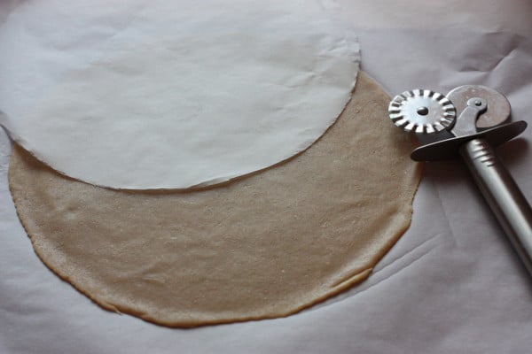 Celé cesto si odvážime (malo by mať 850/860 gramov) a rozdelíme ho na 6 rovnakých kúskov. Na pečiaci papier si obkreslíme kruh v priemere 22 cm a vystrihneme ho. Dáme si nový kus papiera na pečenie, zoberieme si jeden bochník a vyvaľkáme si ho na papieri na tenký kruh. Priložíme náš vystrihnutý kruh a koliečkom orežeme dokola a odstránime presahujúce cesto. Do orezaného kruhu spravíme koliečkom štyri zárezy (čiarky) aby nám pri pečení dýchalo.